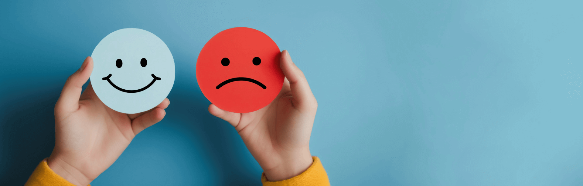 Two round emotion cards held by hands: a blue smiling face and a red frowning face, showing happy vs sad.