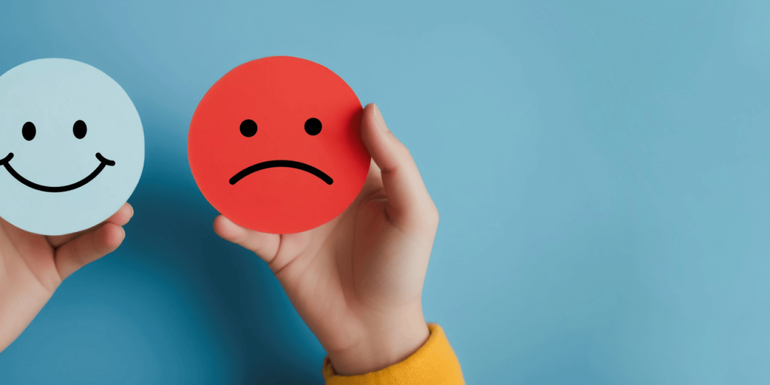 Two round emotion cards held by hands: a blue smiling face and a red frowning face, showing happy vs sad.